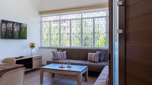 Un salon moderne avec une table basse en bois, un canapé orné de coussins à rayures et une grande fenêtre avec des barreaux en métal.