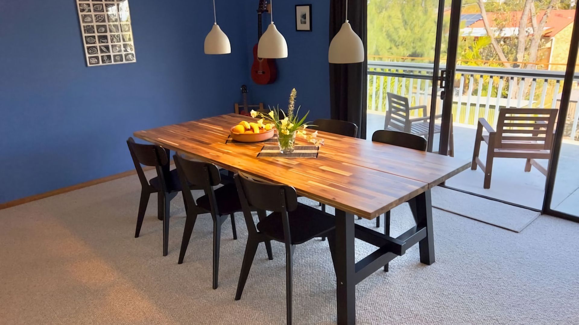 Un coin repas avec une table en bois, des chaises noires et une vue sur l’extérieur grâce à une porte vitrée.