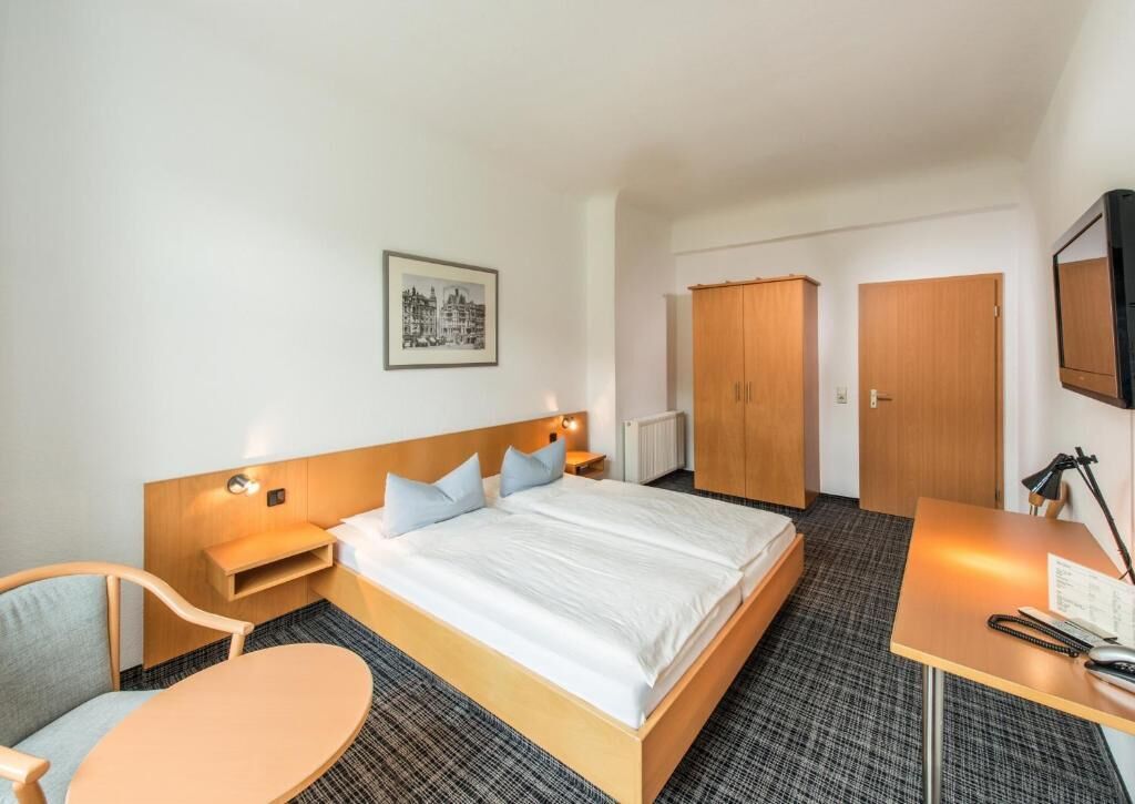 Ein Hotelzimmer mit Bett, Schreibtisch, Stuhl und Kleiderschrank.