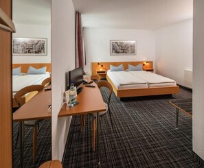 A hotel room with a bed, a desk, a chair, a TV, and a bedside table. - City Hotel (Eisenach)