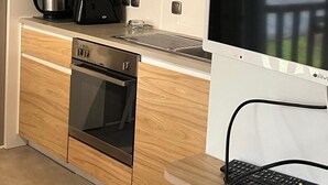 A modern kitchen with wooden cabinets, stainless steel appliances, and a flat-screen TV. - Mobile home in La Palmyre, 10 minutes from the beach, close to the zoo and the Coubre lighthouse (Les Mathes)