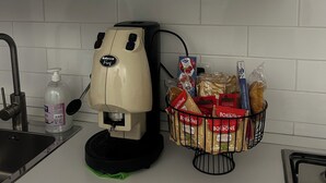 A kitchen with white cabinets, a coffee machine, a sink, and a basket containing bread and snacks. - Nalusa rooms - in downtown Toledo (Napoli)