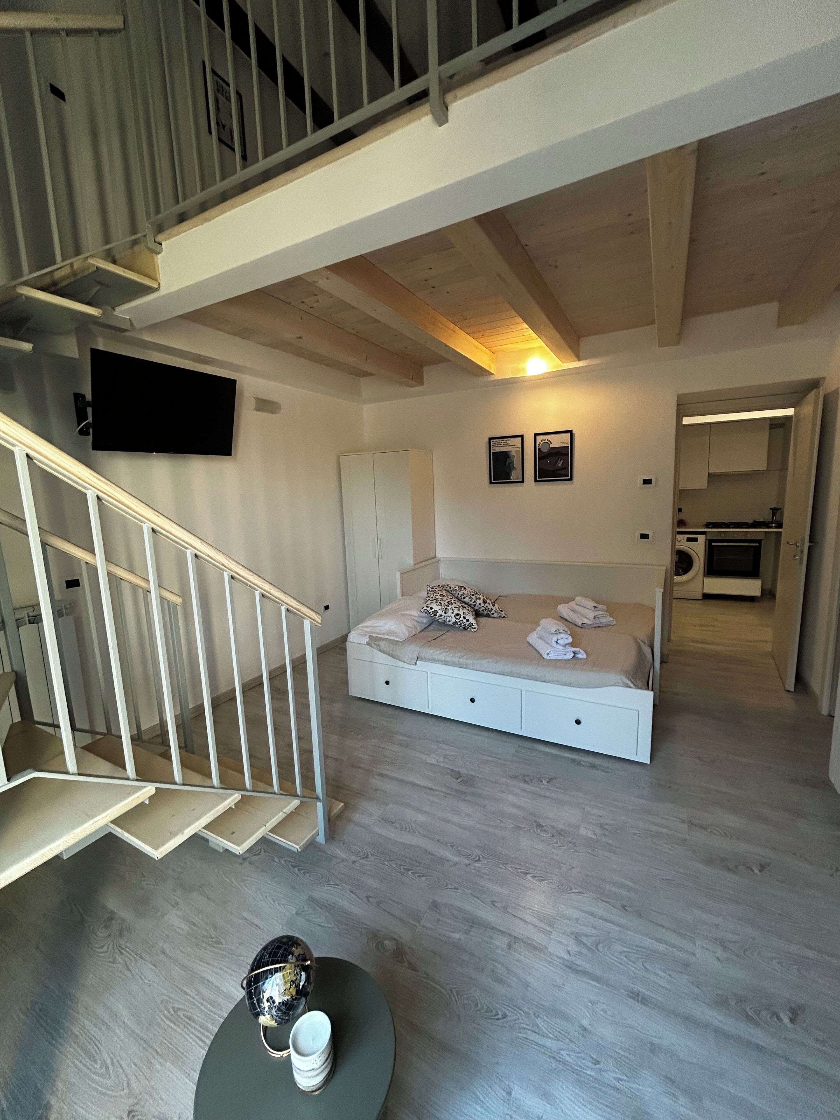 A bedroom with a bed, a TV mounted on the wall, and a staircase leading to an upper level.