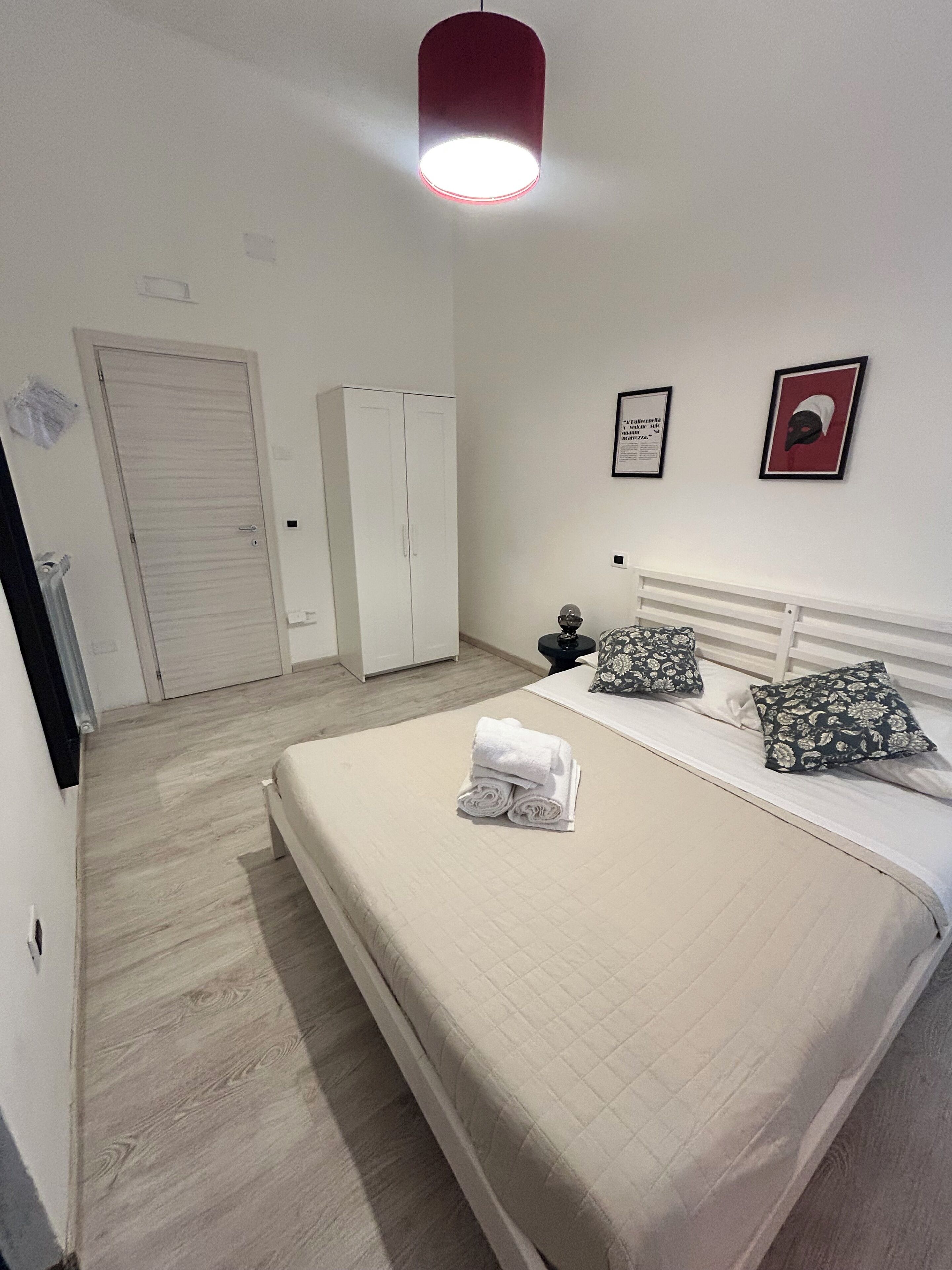 A bedroom with a bed, a wardrobe, a door, and a wall with two framed items.