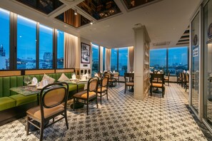 Un restaurant offrant une vue sur la ville, doté de sièges verts et d’un sol à motifs.