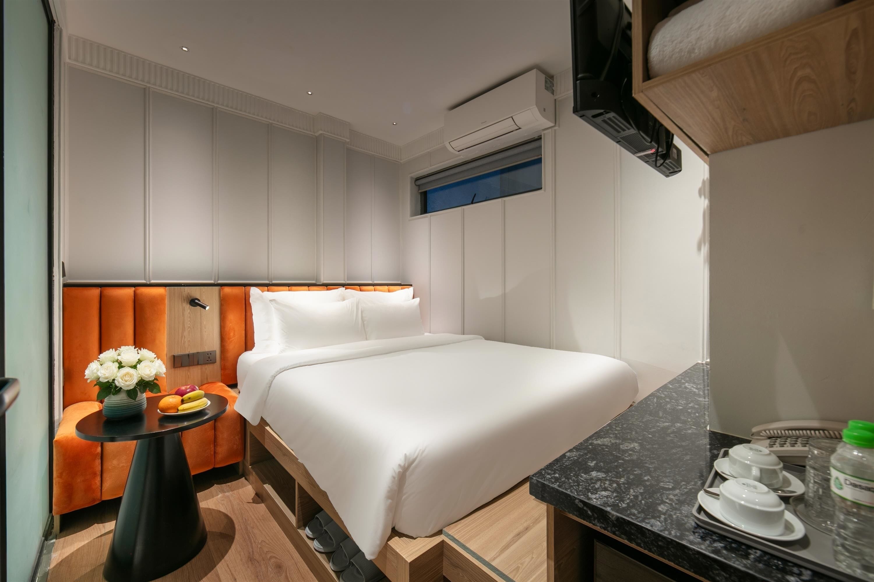 A hotel room with a bed, a small table with a vase of flowers, a mirror, and a bathroom area.