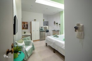 A modern bedroom with a bed, a desk, a chair, a wardrobe, and a kitchenette. - The Mint - Stylish Studio in Egaleo/Athens (Egaleo)