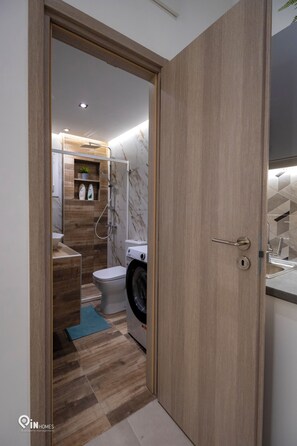A modern bathroom with a wooden vanity, a toilet, and a washing machine. - The Mint - Stylish Studio in Egaleo/Athens (Egaleo)