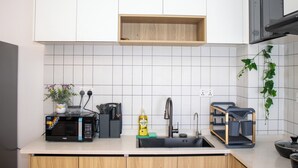 Eine moderne Küche mit weißen Schränken, einer schwarzen Mikrowelle, einem Spülbecken und einem Holzregal darüber.