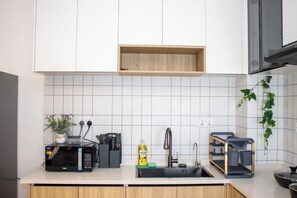Et moderne køkken med hvide skabe, en sort mikrobølgeovn, en vask og en træhylde over.