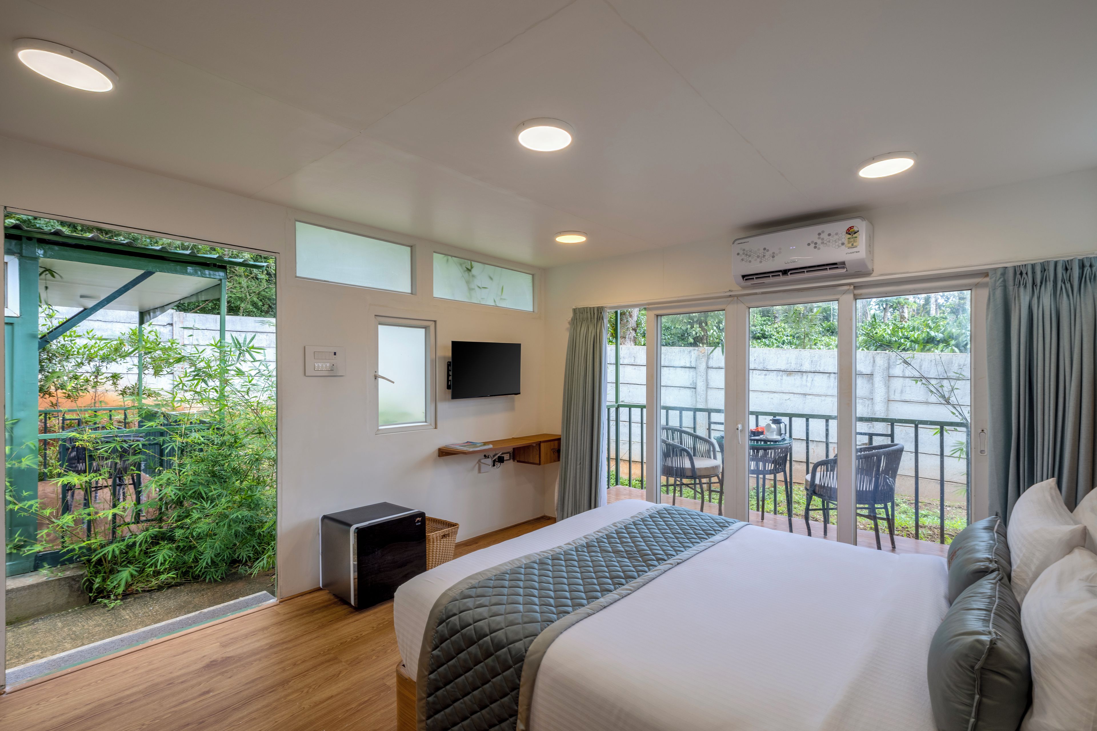 Una habitación de hotel con cama, televisión, escritorio y balcón con sillas.