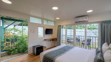 Una habitación de hotel con cama, televisión, escritorio y balcón con sillas.