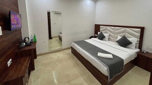 A modern hotel room with a large bed, a TV mounted on the wall, a desk with a chair, and a mirror. - Hotel Ganga Palace (Agra)