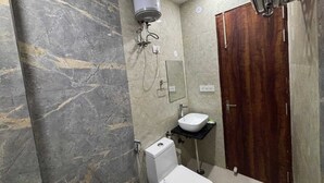 A bathroom with a marble wall, a white toilet, a sink, and a shower. - Hotel Ganga Palace (Agra)