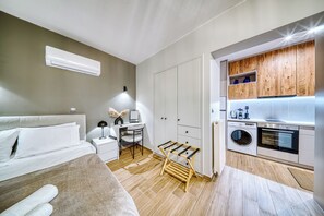 A compact bedroom with a bed, bedside table, and a desk with chair. A small laundry area with a washing machine and dryer is adjacent to the bedroom.