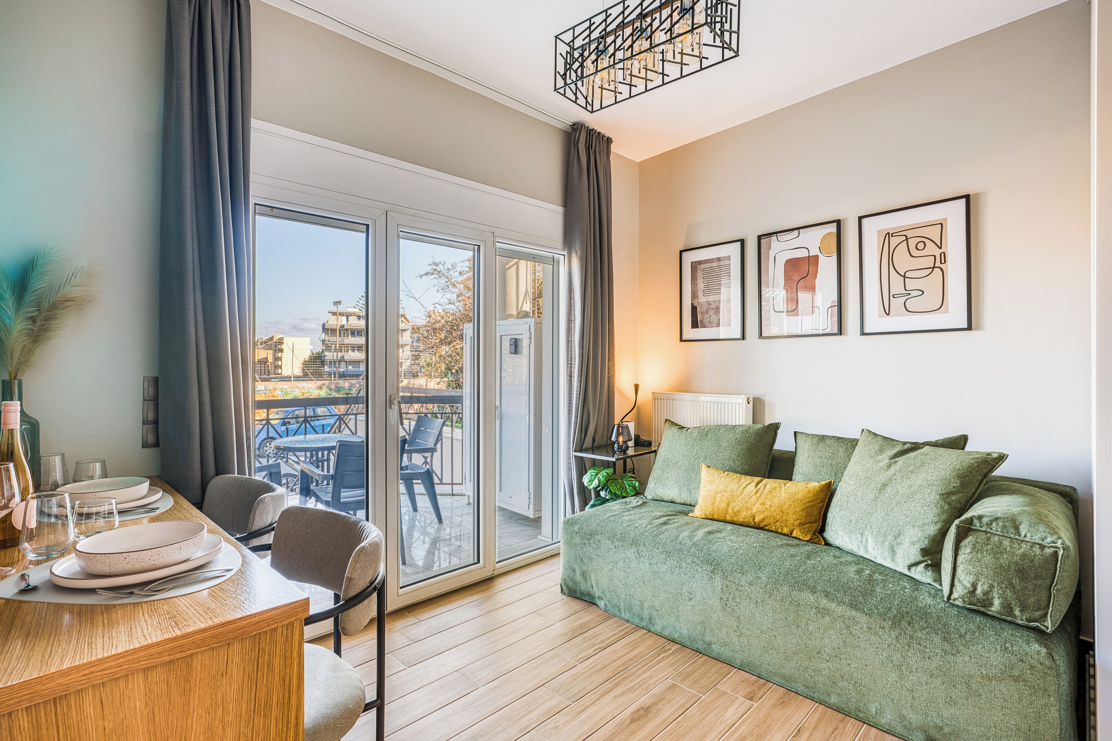 Een moderne woonkamer met een groene bank, een eettafel met borden en glazen, en een balkon met uitzicht op gebouwen.