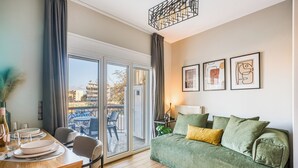 Un saló modern amb un sofà verd, una taula de menjador amb plats i gots, i un balcó amb vista a edificis.