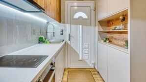 Una cuina moderna amb taulell blanc, forn integrat i armari de fusta.