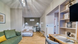 Habitació d'hotel senzilla amb llit, sofà, escriptori i cadira, i televisió sobre una prestatgeria.