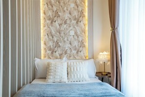 Una cama bien hecha con una manta azul, una pared con un estampado de hojas y una lámpara de noche.