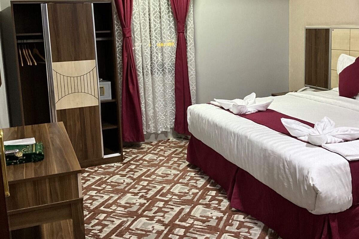 A hotel room with a bed, a wardrobe, a desk, and a patterned carpet.
