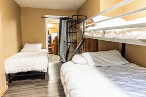 Une chambre avec deux lits superposés, un plancher en bois et une porte donnant sur un couloir.