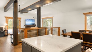 A spacious kitchen with a marble countertop, wooden beams, and large windows.