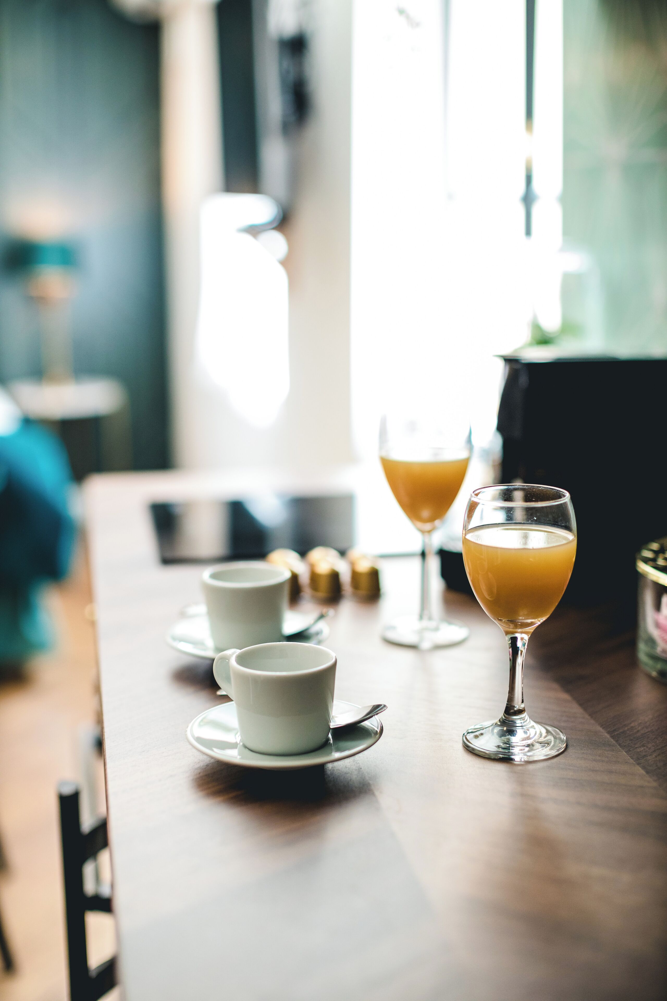A table with two glasses of orange juice and two white cups with saucers, suggesting a breakfast setting.
