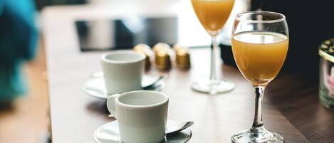 A table with two glasses of orange juice and two white cups with saucers, suggesting a breakfast setting.