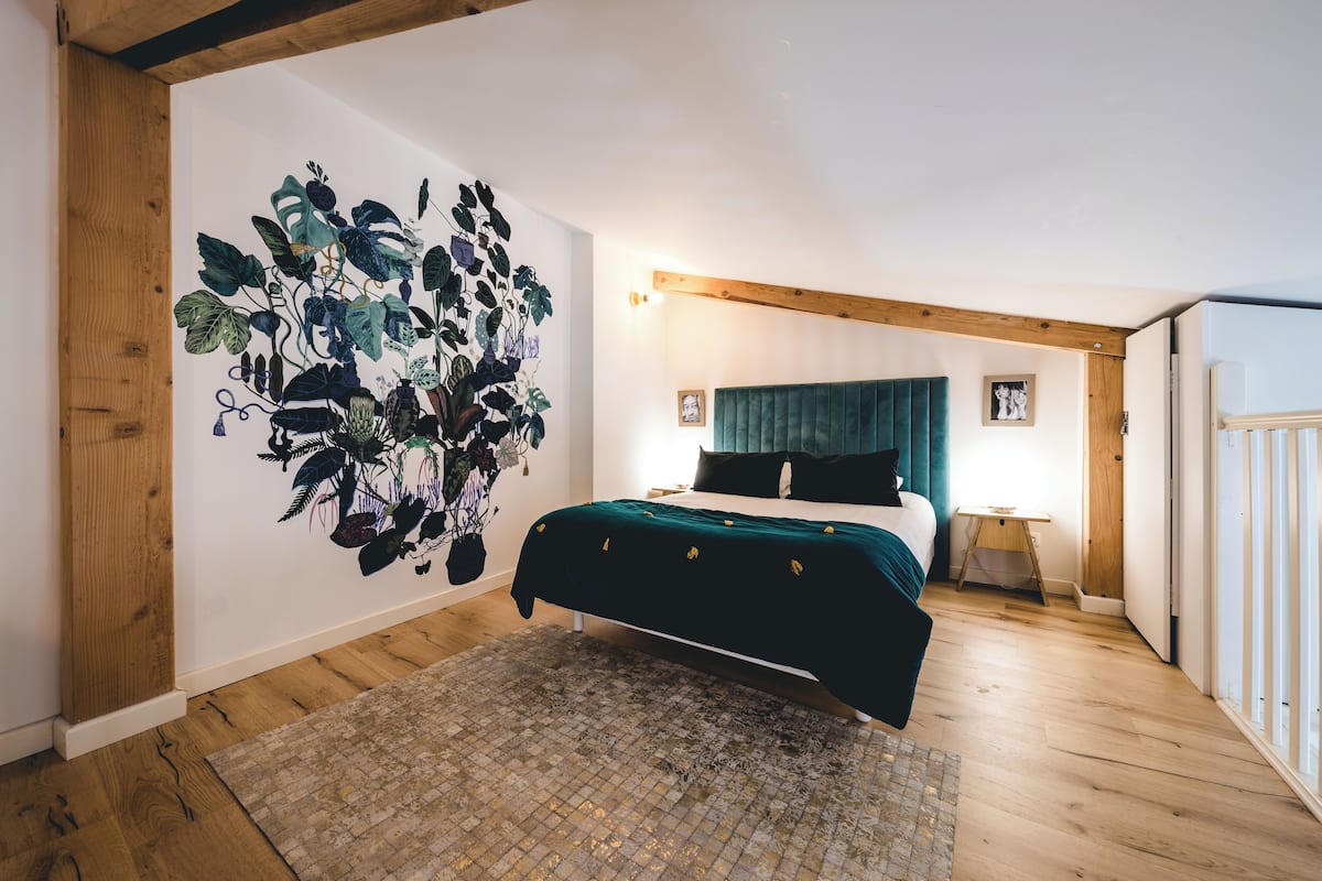 A bedroom with a bed, a large wall mural, and a wooden floor.