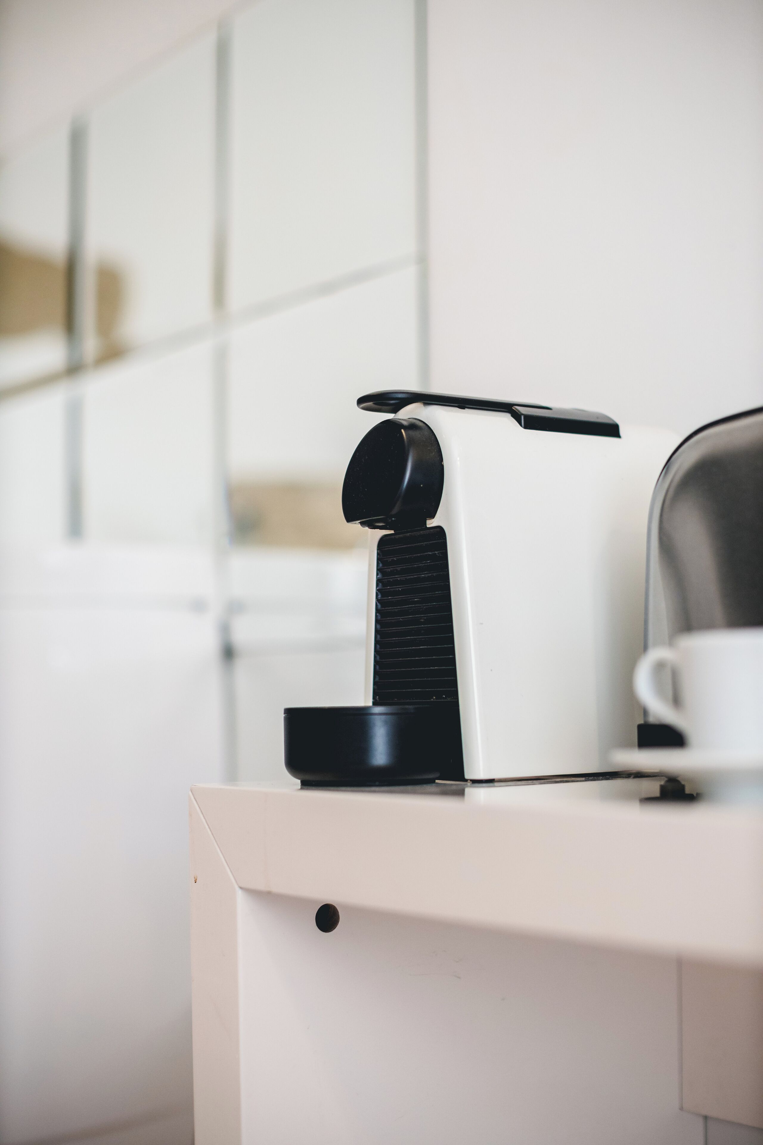 Une machine à café sur un comptoir blanc, avec une tasse et un verre.