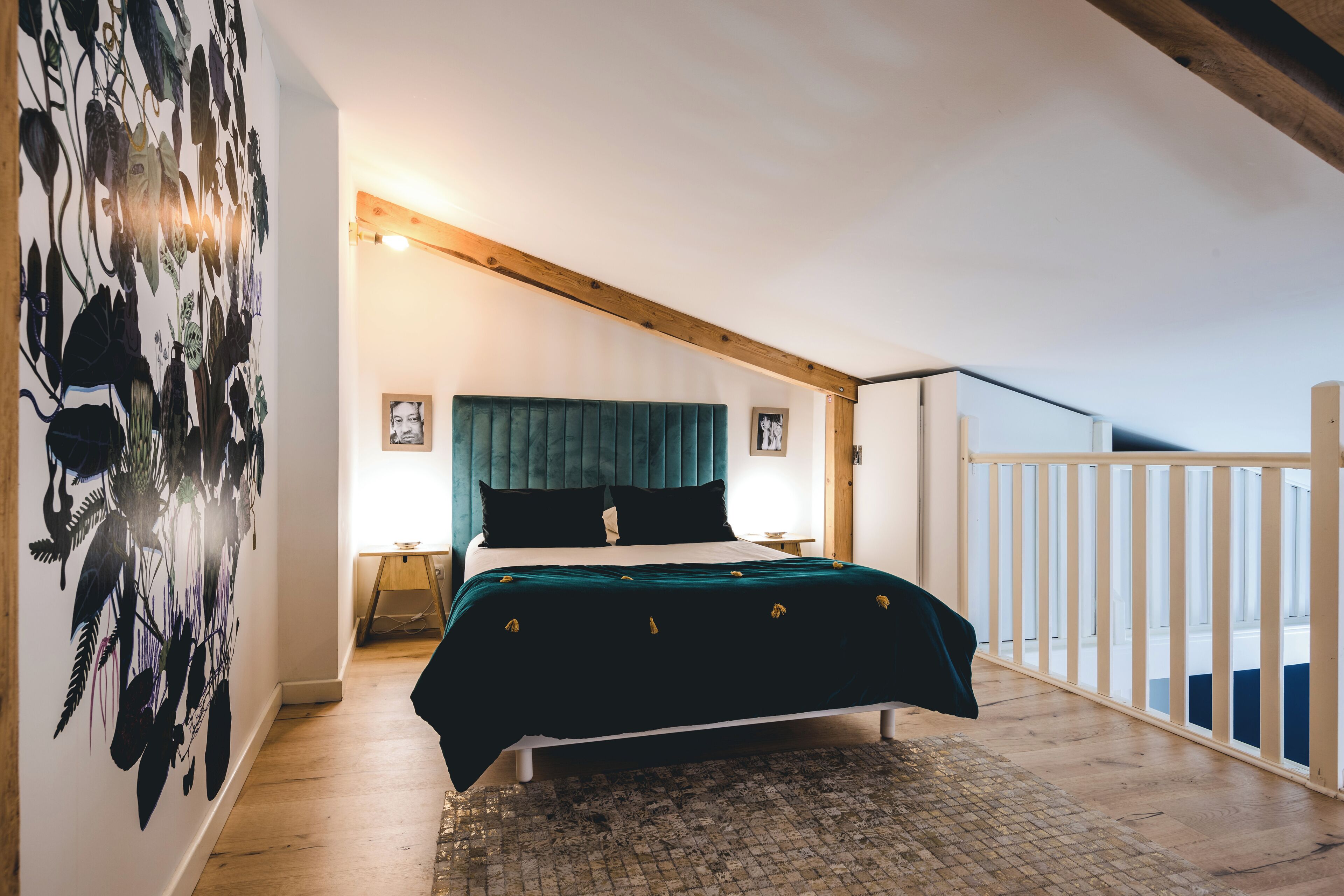 Un dormitorio con cama, techo de madera, barandilla de balcón y pared con diseño de hojas.