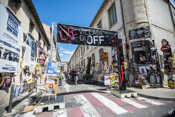 Vista da rua com uma placa grande que diz 'OFF VILLAGE DUFF' e diversos cartazes e faixas nas construções.