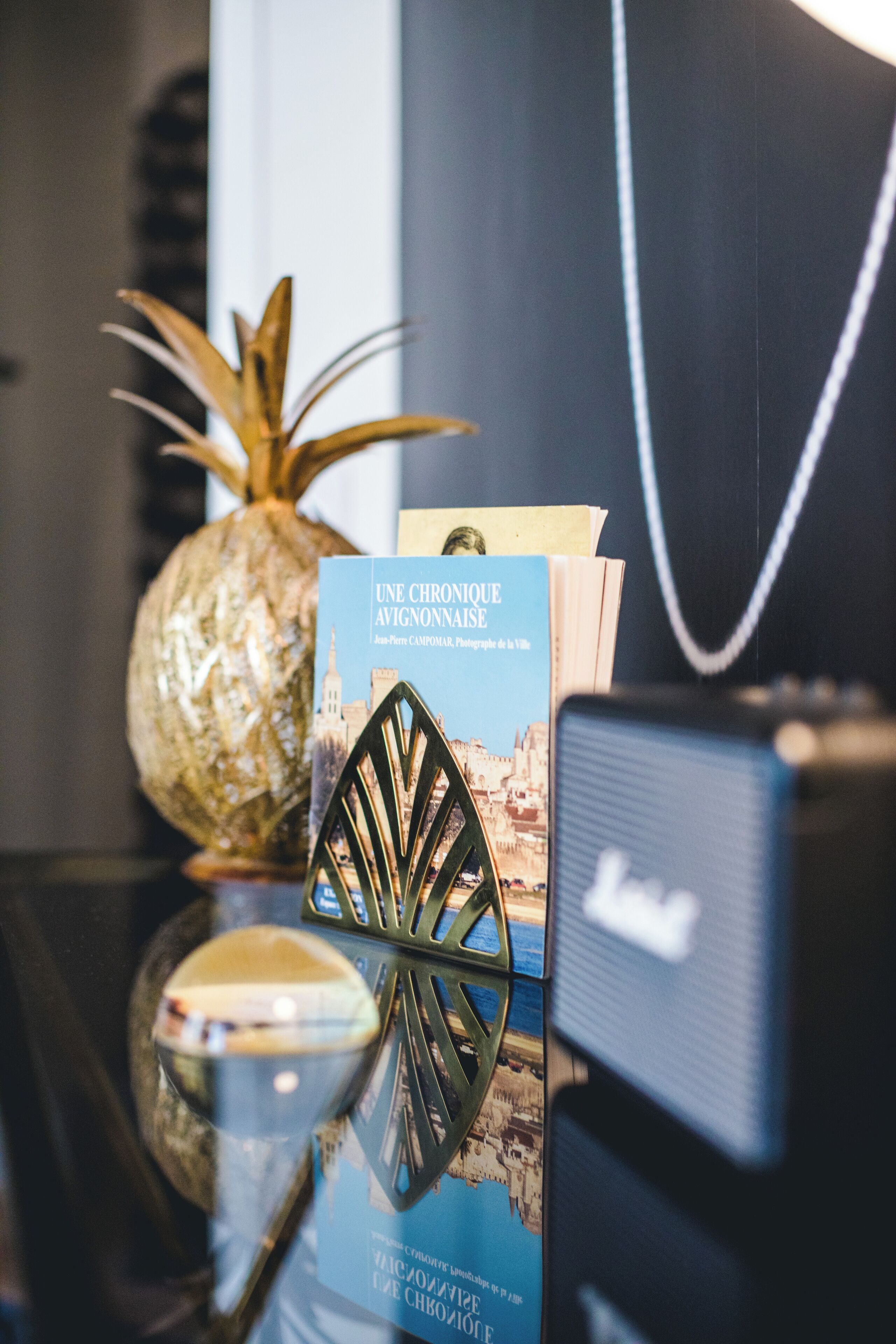 Un livre intitulé « Une chronique d’Avignon » est posé sur une table, à côté d’un ananas et d’un objet décoratif en métal.