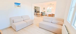 A modern living room with two beige sofas, a dining area with wooden furniture, and a kitchen in the background. - Villa Graine des pins, 14 people, near the ocean (Biscarrosse)