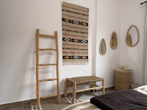 Une pièce avec une échelle en bois, un banc en osier, une décoration murale à motifs et deux miroirs ronds.