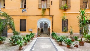 Un patio con un sendero central flanqueado por plantas en macetas y un edificio con una entrada arqueada.