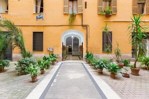 A courtyard with a central pathway flanked by potted plants and a building with an arched entrance. - Trastevere Lovely House - Historic Charm and Modern Comfort in the Heart of Rome (Roma)