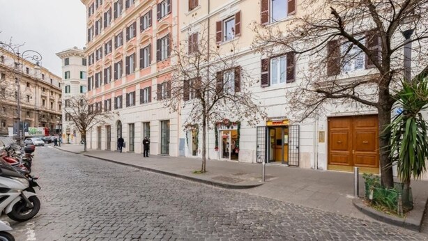 Una calle adoquinada flanqueada por edificios de varios pisos, algunos con escaparates y letreros visibles.