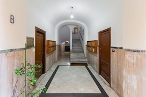 Un couloir doté d’un sol en marbre, de portes en bois et d’un escalier menant à l’étage supérieur.