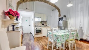 Una cocina amplia con piso de madera, armarios blancos y un comedor con mantel floral.
