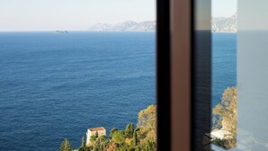 A coastal view with a clear blue sea, distant mountains, and a building with a sloped roof. - Sea Whisper Home -Sunset, Sea, Easy Stay, Shops (Praiano)