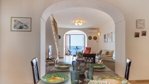 A dining area with a table set for four, a view of the living room, and a balcony in the background. - Sea Whisper Home -Sunset, Sea, Easy Stay, Shops (Praiano)