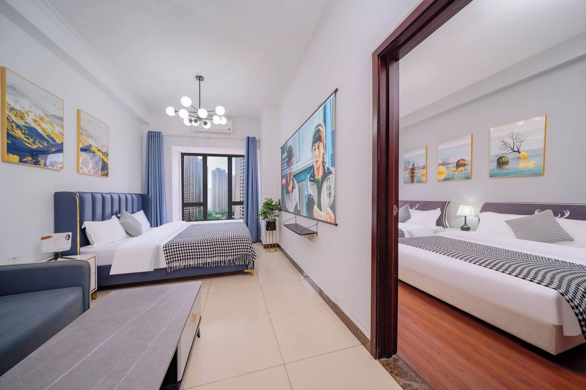 Habitación de hotel con dos camas, un sofá, un escritorio y un ventanal con vistas a la ciudad.