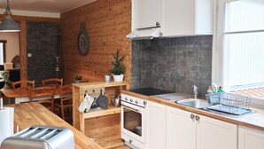 A modern kitchen with wooden flooring, white cabinets, a built-in oven, a sink, and a dining area with a wooden table and chairs. - Mountain Chalet Hiking, Nature, Skiing near Gérardmer (Le Valtin)