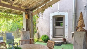 A covered patio with a wooden table and chairs, a stone wall, and a small garden. - Mountain Chalet Hiking, Nature, Skiing near Gérardmer (Le Valtin)