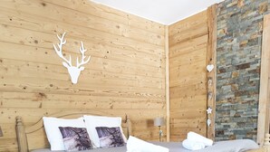 A wooden bed with a headboard, a nightstand, and a wall with a wooden panel and a stone accent wall. - Mountain Chalet Hiking, Nature, Skiing near Gérardmer (Le Valtin)