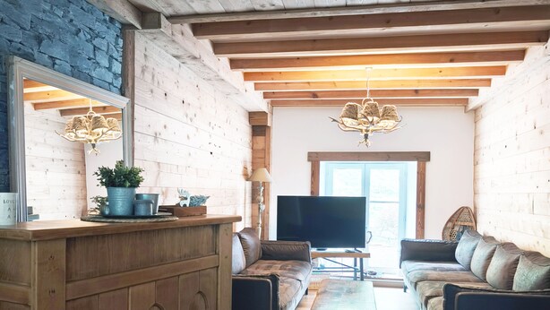 A rustic interior with exposed wooden beams, a stone wall, a wooden bar, a sofa, and a television. - Mountain Chalet Hiking, Nature, Skiing near Gérardmer (Le Valtin)