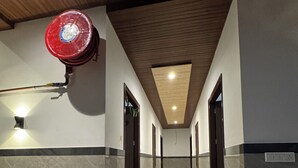 A hotel corridor with marble walls, wooden ceiling, and a red fire extinguisher. - Hotel Utsav (Khatima)