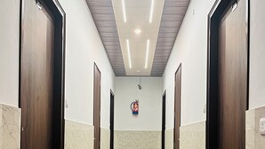 A hallway with marble flooring, wooden doors, and a fire extinguisher mounted on the wall. - Hotel Utsav (Khatima)